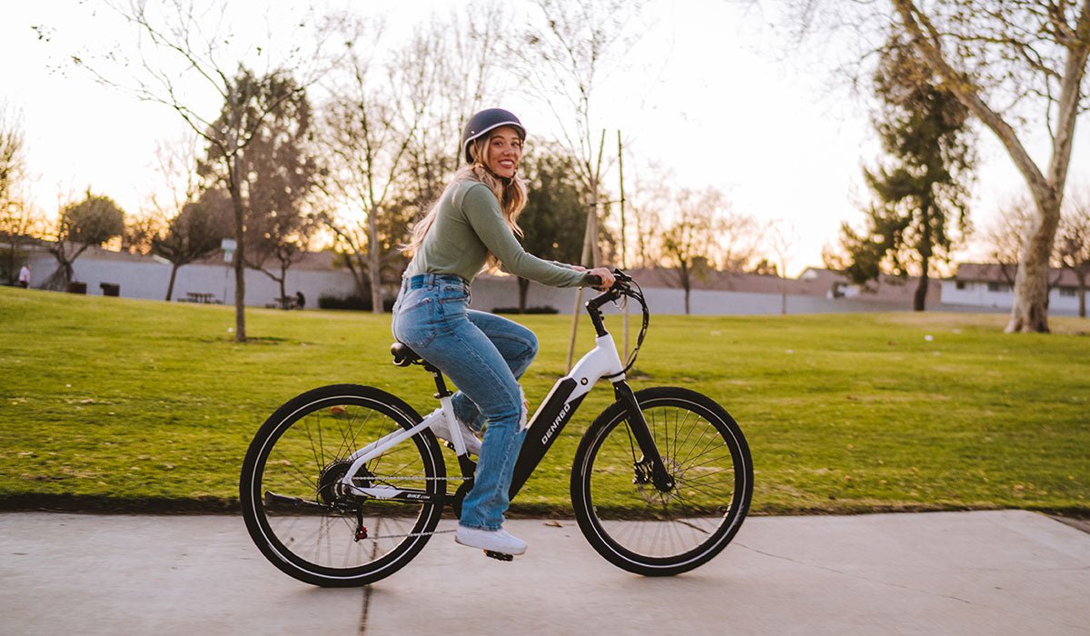 A woman riding a Denago City 1 Step-Thru Electric Bike with a 7 speed shifter and an adjustable stem.