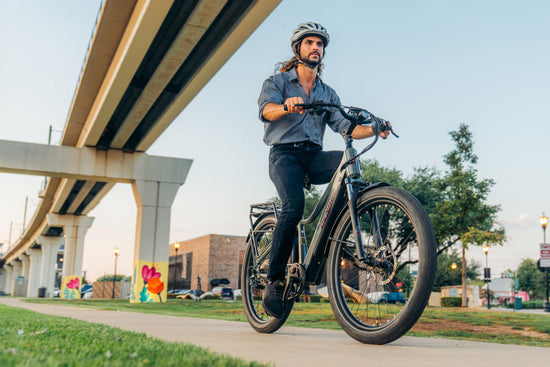 Man riding an electric commuter ebike on a pedestrian bike trail under a bridge.