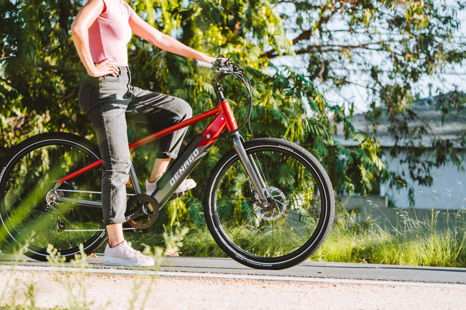 Woman sitting on eBike displaying the Denago logo with bushes in the background.