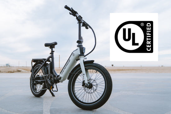 Folding electric bike near the beach with the UL Certified Logo overlaid.